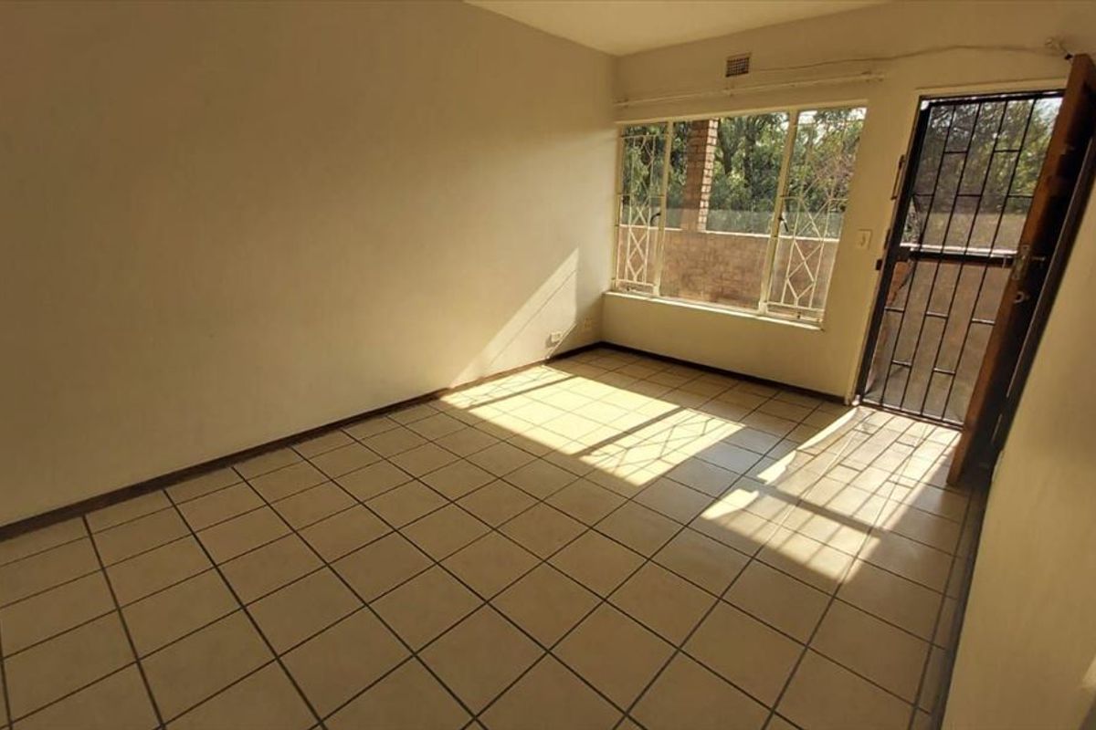An empty living room featuring tiled flooring, a large window with security bars, and a secure metal entrance gate.