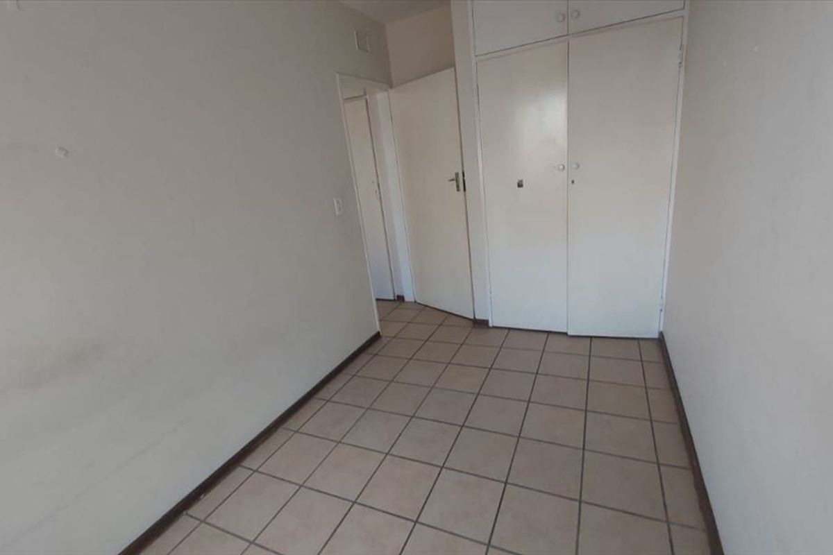 An empty bedroom featuring tiled flooring and built-in cupboards, presenting a blank canvas for potential renovation or staging.