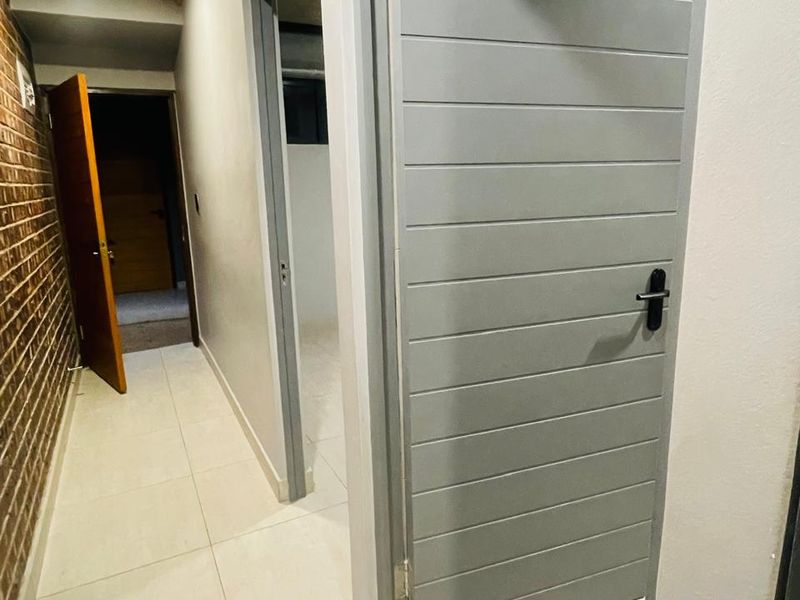 A clean, modern hallway featuring light-colored floor tiles and an exposed brick feature wall, providing access to multiple rooms.