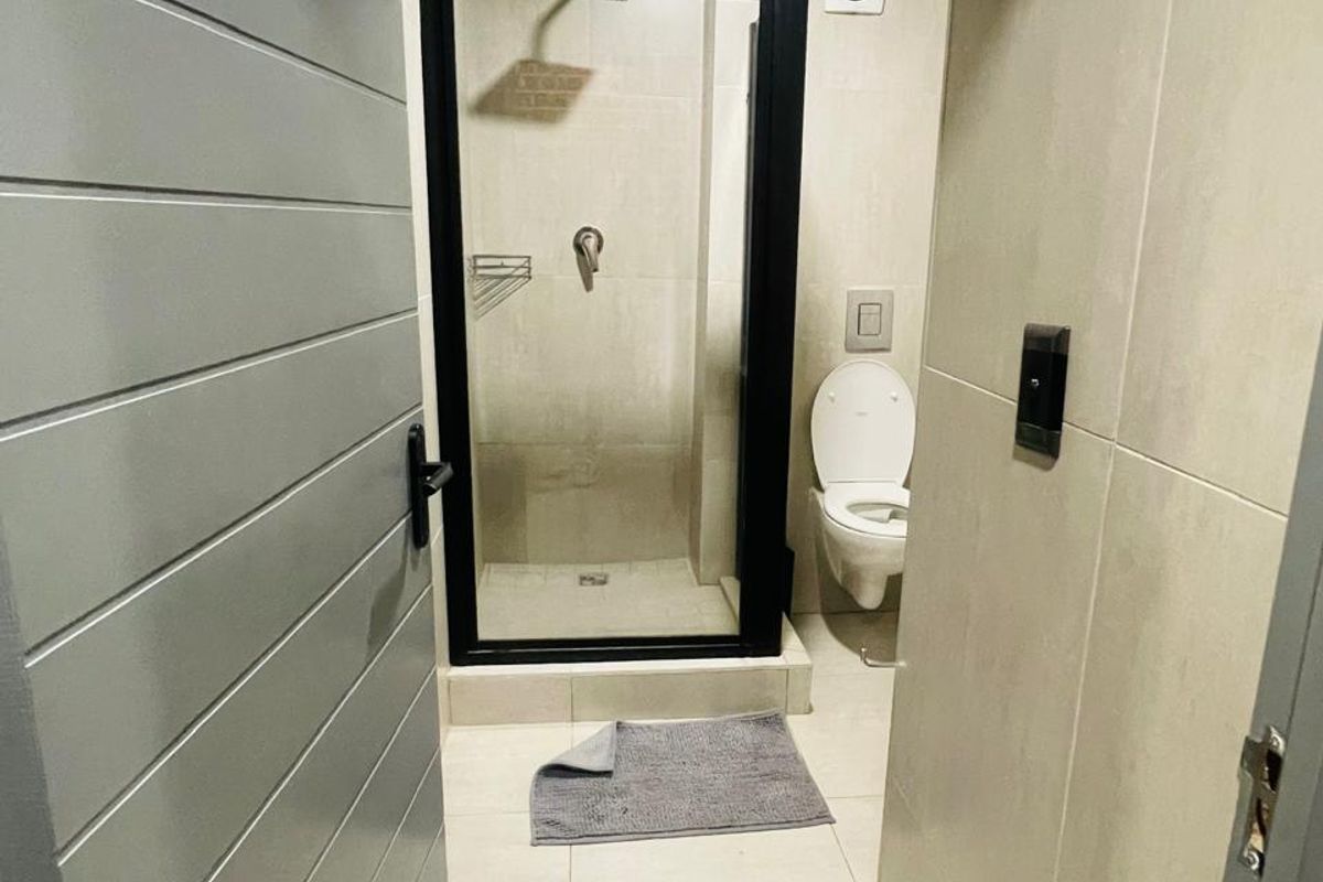 A modern, clean bathroom featuring a glass-enclosed shower, wall-mounted toilet, and neutral floor-to-ceiling tiling.