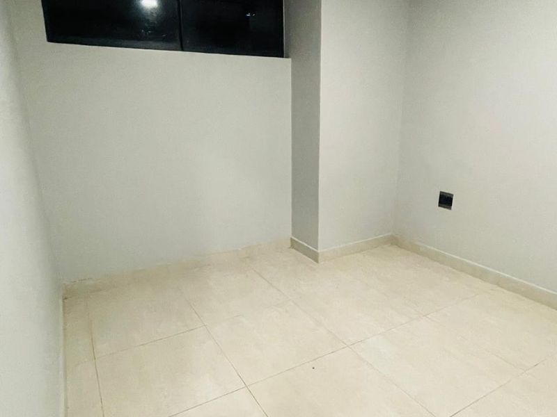 A clean, empty bedroom featuring neutral tiled flooring and a high-level window, providing a blank canvas for personalization.