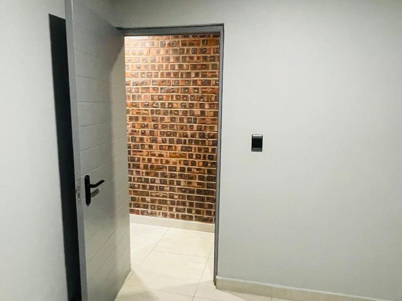 A clean, empty hallway featuring light-colored floor tiles and a contrasting exposed brick wall visible through an open doorway.