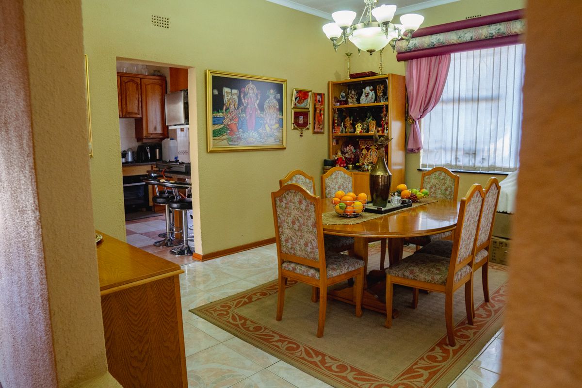 A dining room featuring tiled flooring and an archway leading to the kitchen, with natural light provided by a window with a pelmet.