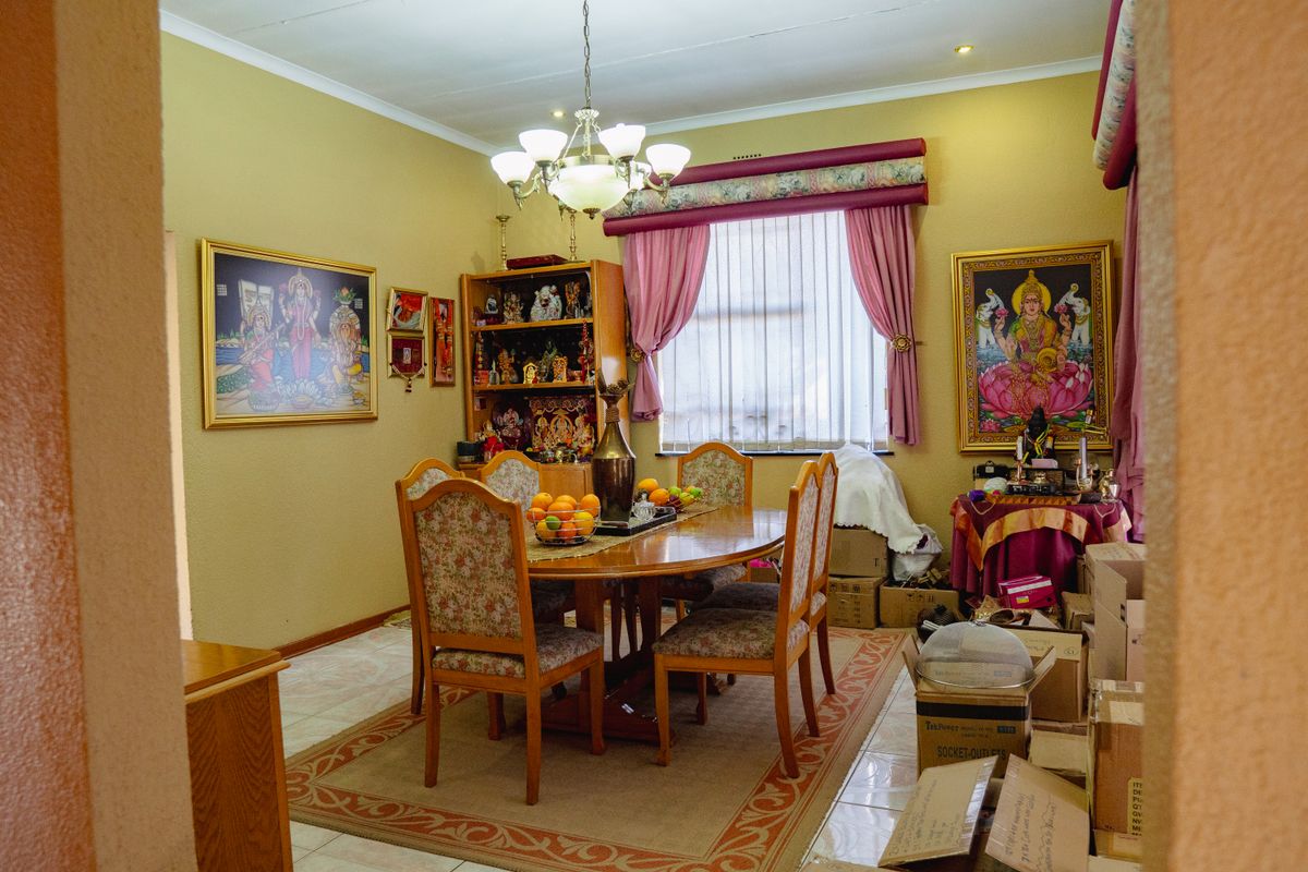 A dining room featuring tiled flooring, a central chandelier, and a window with a decorative pelmet, providing a functional space for family meals.