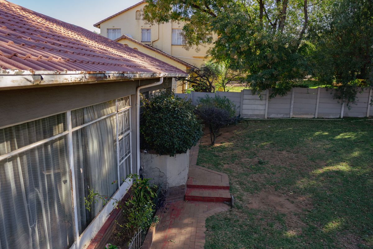 Rear exterior view of the property featuring a tiled roof, paved walkway, and a private garden enclosed by a precast concrete boundary wall.