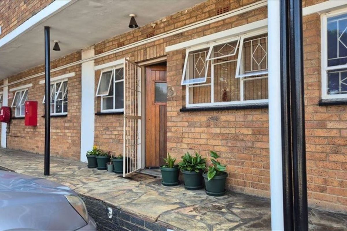 Exterior view of an apartment entrance featuring a brick facade, security gate, timber door, and stone paved walkway.