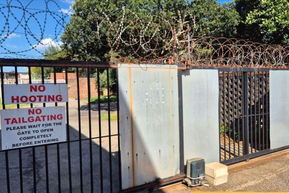 Secure gated entrance featuring a sliding metal gate with razor wire topping and automated gate motor system.