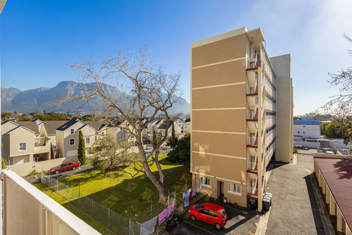 Exterior view of the apartment building featuring brick facade, external stairwell, and balconies, set against a mountain backdrop with surrounding grounds.