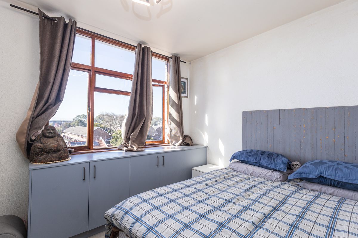 A bedroom featuring built-in storage cabinetry beneath large timber-framed windows, offering natural light and an elevated view.