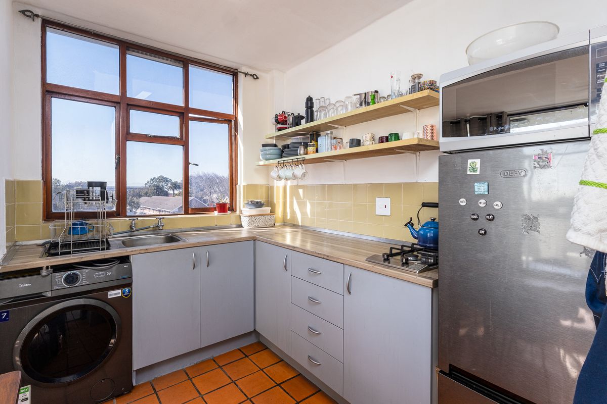 A functional kitchen featuring laminate countertops, a gas hob, stainless steel sink, and open shelving, with large windows providing natural light.