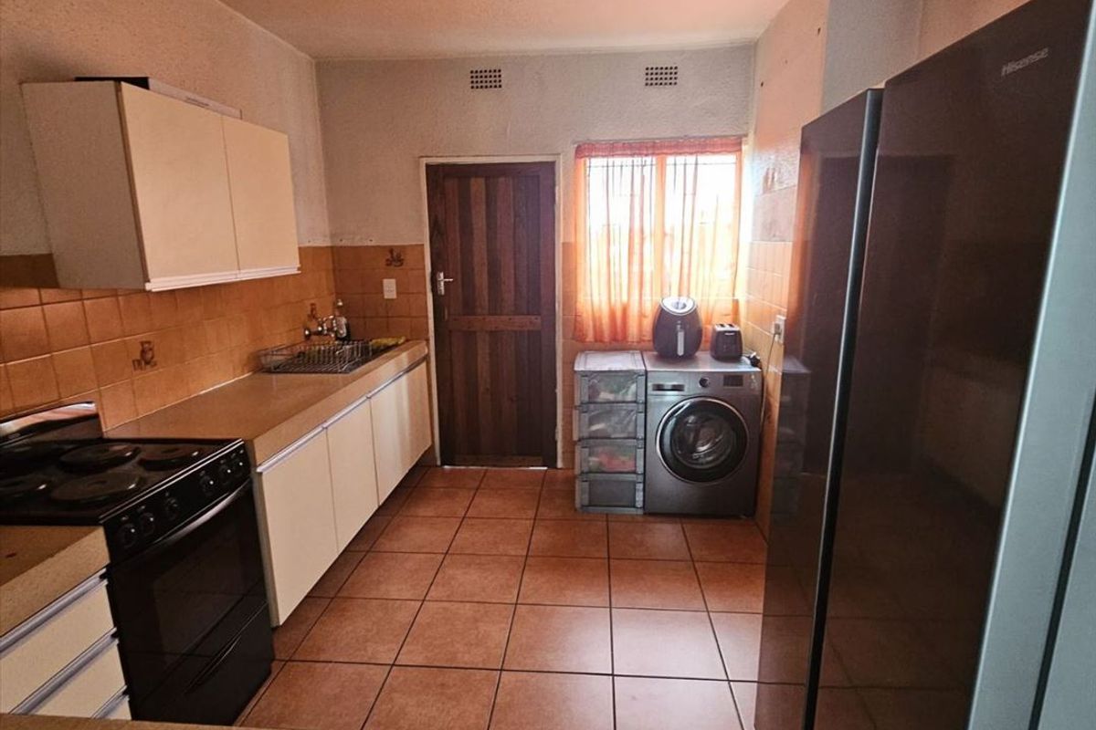 A functional kitchen featuring tiled flooring, built-in cabinetry, and a tiled splashback, offering a practical layout with direct access to an exterior door.
