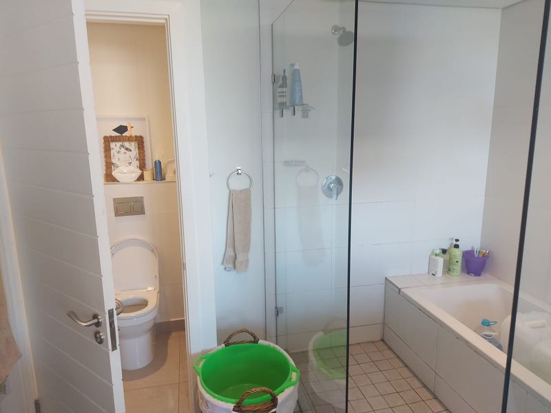 A modern bathroom featuring a glass-enclosed shower, a built-in bathtub, and a separate enclosed toilet area with neutral tiling.