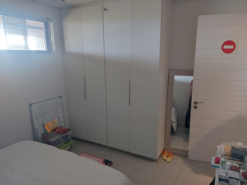 A bedroom featuring a large white built-in wardrobe, tiled flooring, and a modern horizontal panel door.