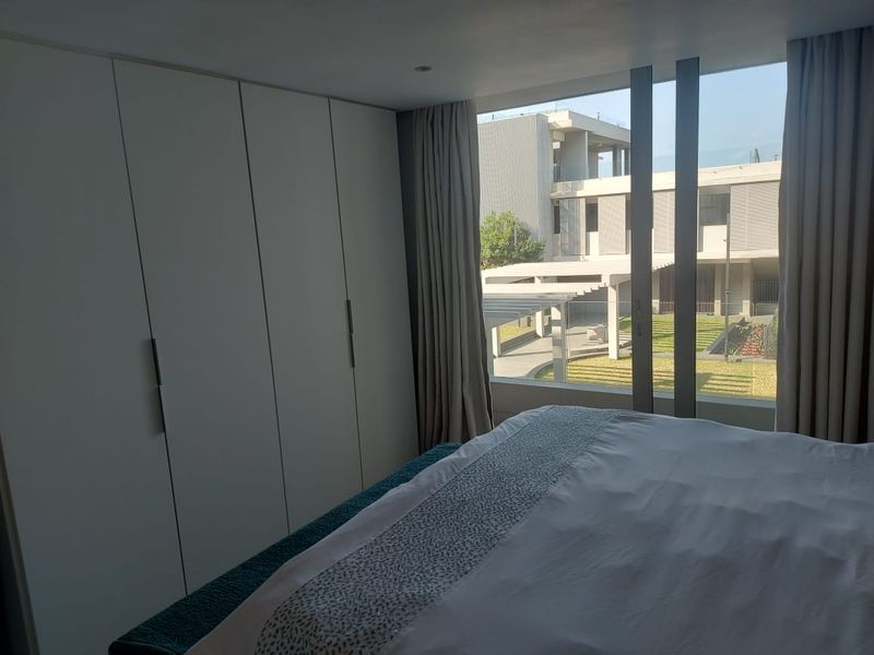 A modern bedroom featuring floor-to-ceiling windows with views of the complex grounds and ample built-in cupboard storage.