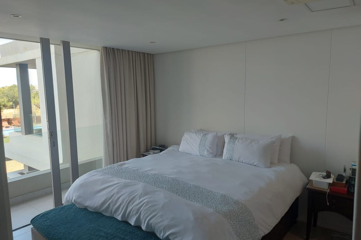 A bright, modern bedroom featuring recessed lighting, ducted air conditioning, and large sliding glass doors providing access to a private balcony.