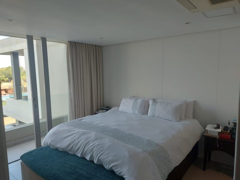A bright, modern bedroom featuring recessed lighting, ducted air conditioning, and large sliding glass doors providing access to a private balcony.