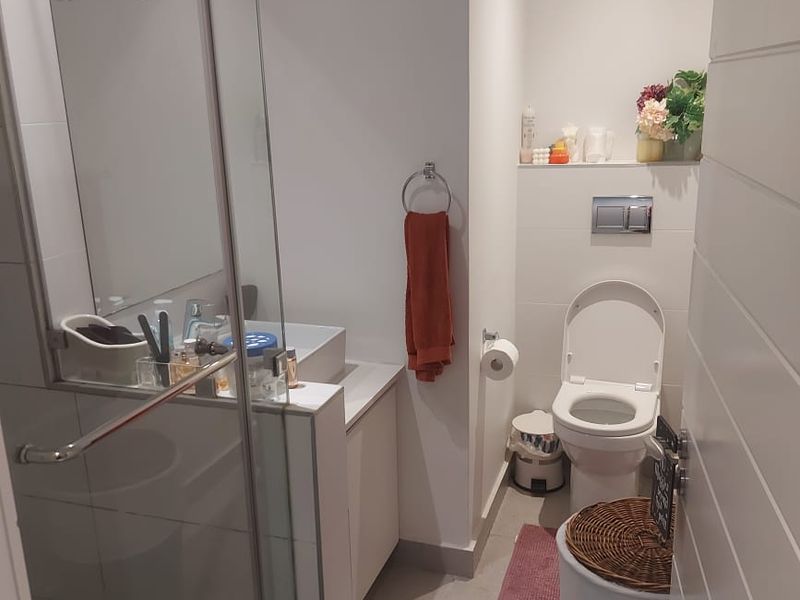 A compact, modern bathroom featuring a glass-enclosed shower, wall-mounted toilet, and a vanity cabinet with clean, neutral finishes.