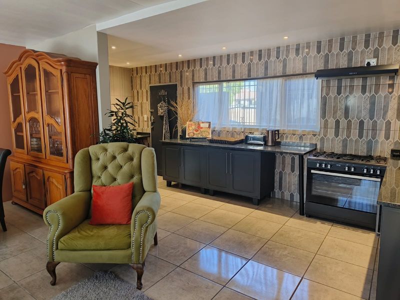Open-plan kitchen area featuring dark cabinetry, granite countertops, a gas stove with extractor, and modern decorative wall tiling throughout the cooking space.