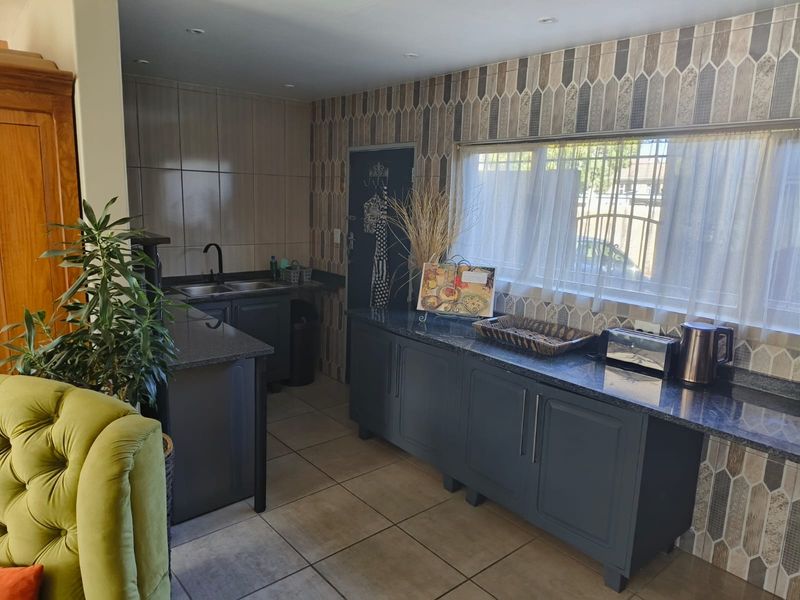 A functional kitchen featuring dark cabinetry, granite countertops, a double basin sink, and decorative tiled backsplash with ample natural light.