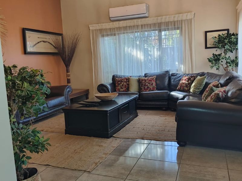 Spacious living room featuring a vaulted ceiling with exposed beams, tiled flooring, and a wall-mounted air conditioning unit.