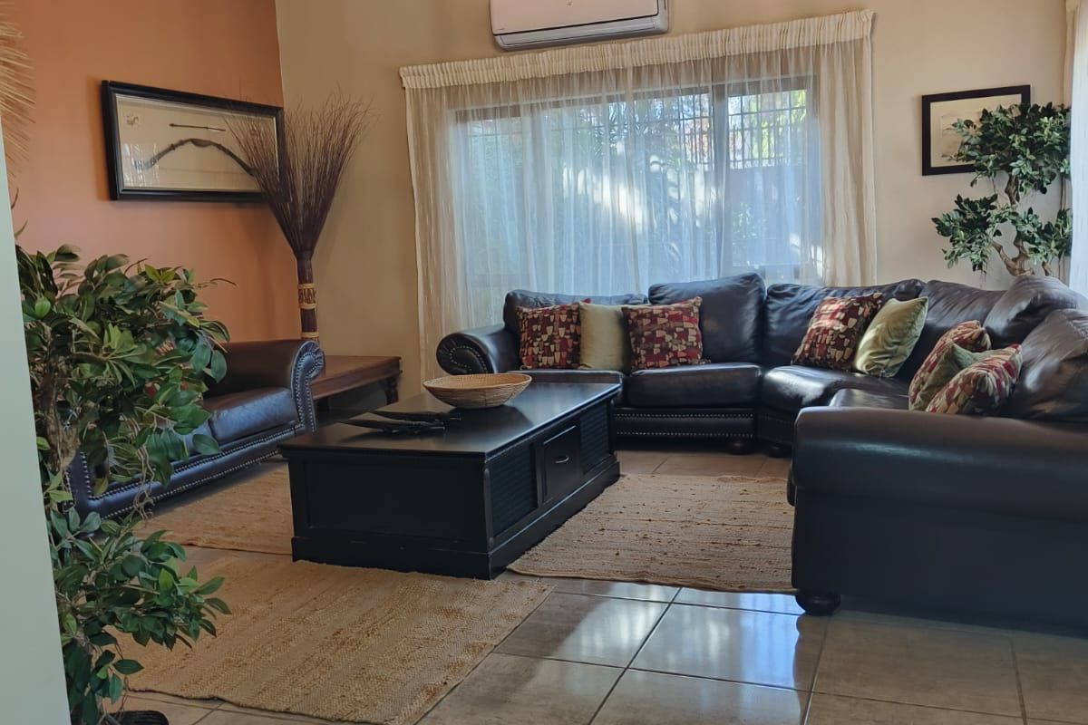 Spacious living room featuring a vaulted ceiling with exposed beams, tiled flooring, and a wall-mounted air conditioning unit.