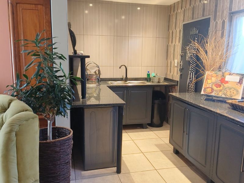 A functional kitchen area featuring dark grey cabinetry, granite countertops, a stainless steel sink, and neutral tiled flooring with recessed lighting.