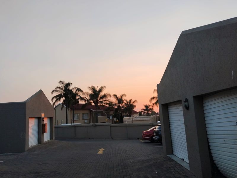 Exterior view of a townhouse complex driveway featuring multiple garage units and perimeter walling at sunset.