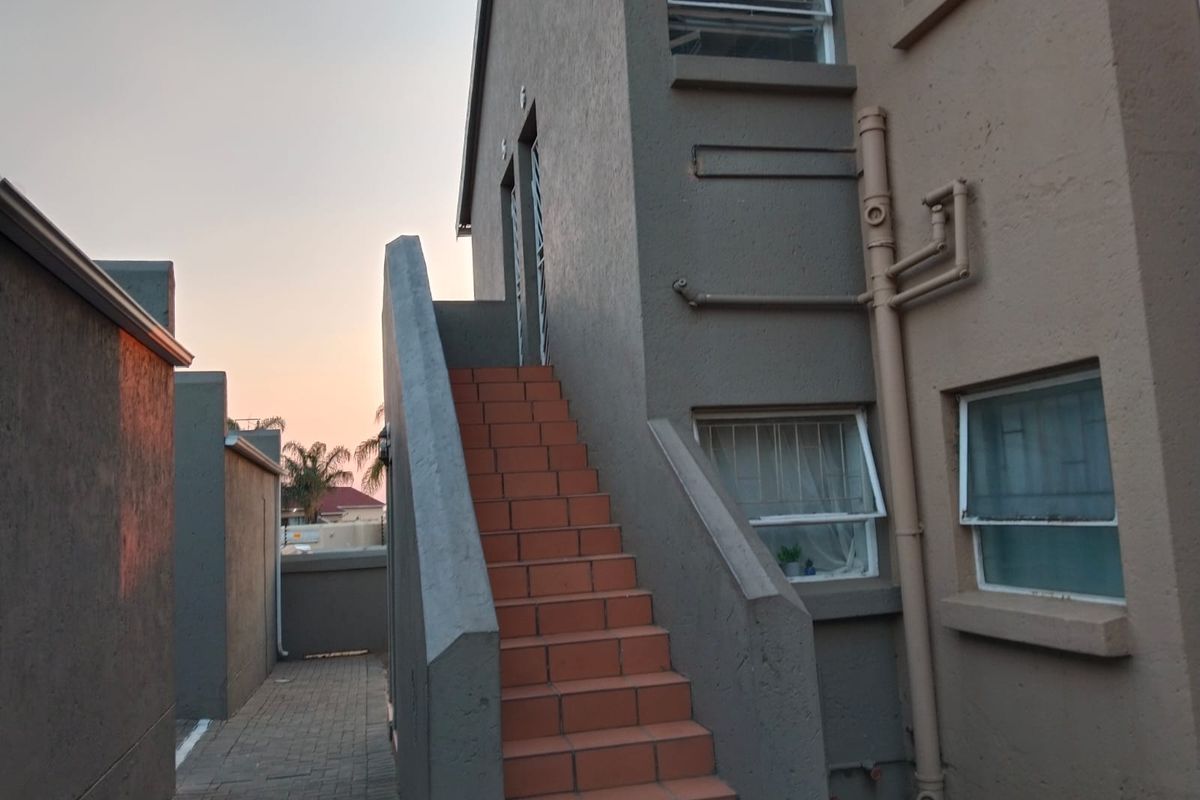 Rear exterior view of the townhouse featuring an external staircase with tiled steps, security-fitted windows, and paved access path.