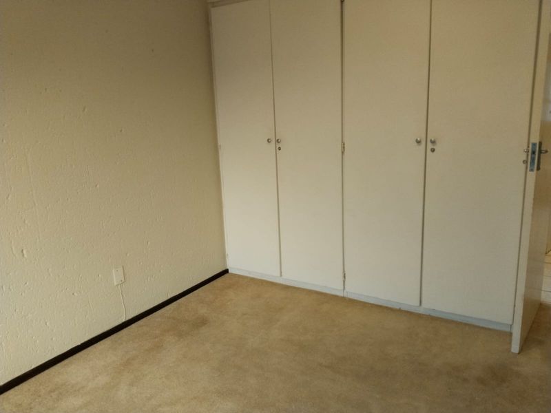 An empty bedroom featuring built-in cupboards and carpeted flooring, offering a blank canvas for potential renovation or interior design updates.