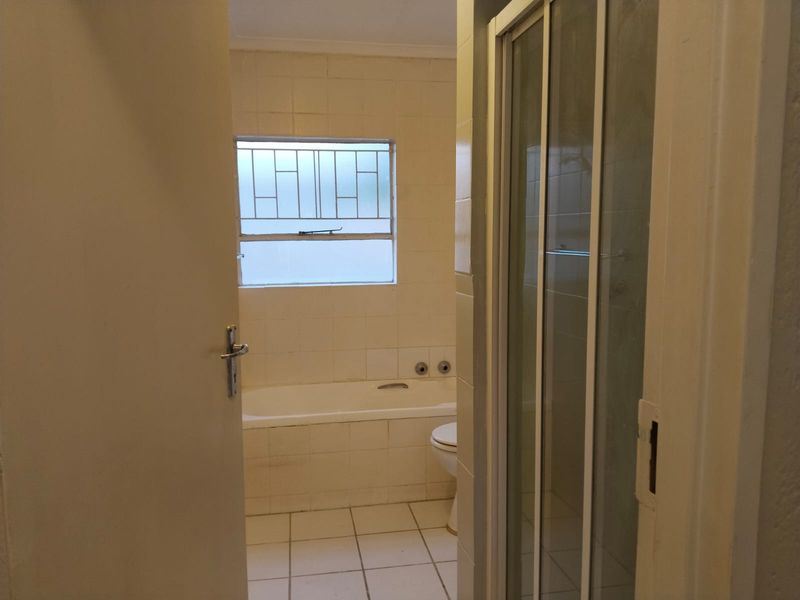 A dated bathroom featuring a bathtub, separate shower enclosure, and toilet, with original wall and floor tiling.