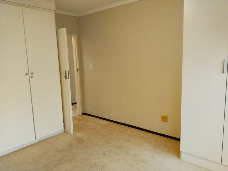 An empty bedroom featuring neutral walls, carpeted flooring, and built-in cupboards, providing a blank canvas for personalization.