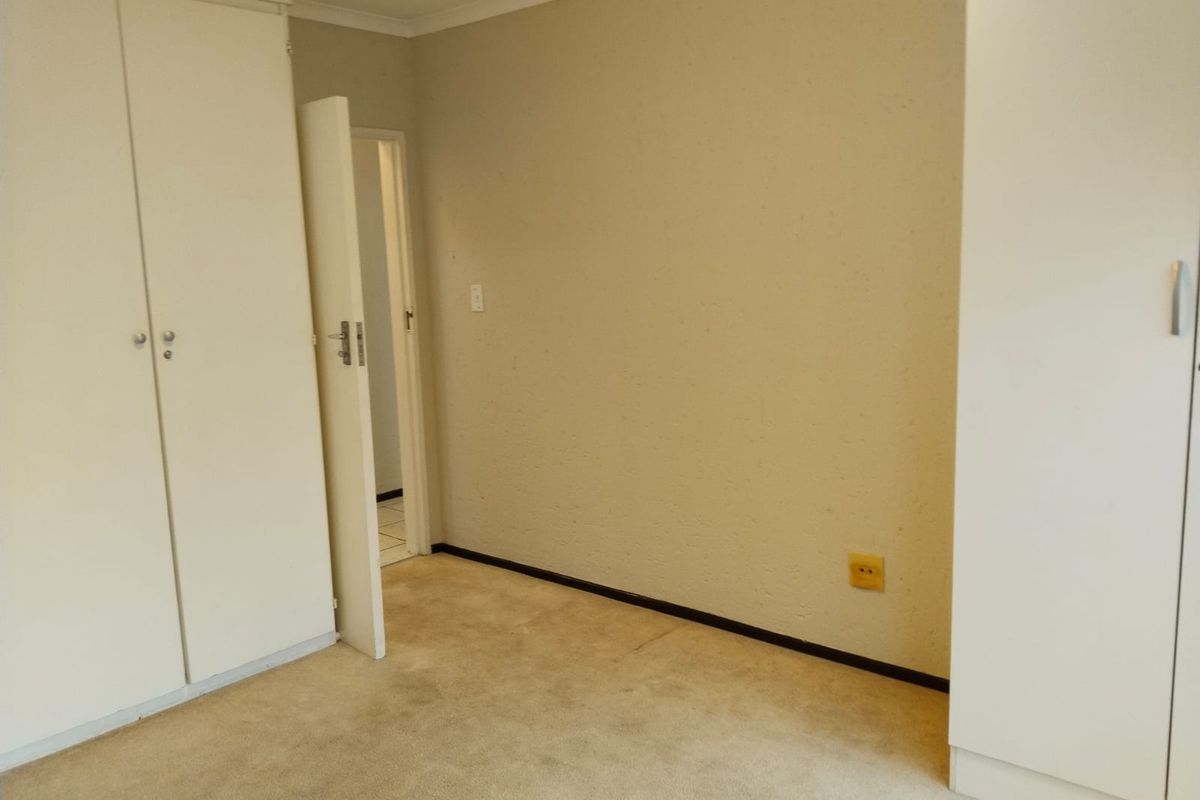 An empty bedroom featuring neutral walls, carpeted flooring, and built-in cupboards, providing a blank canvas for personalization.