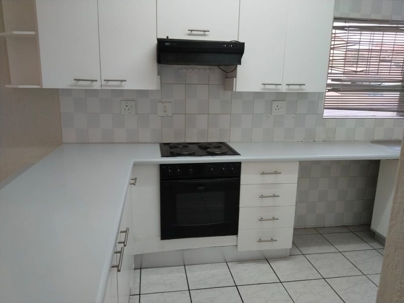 A functional kitchen featuring white cabinetry, laminate countertops, a built-in oven, electric hob, and tiled splashback with neutral ceramic floor tiles.