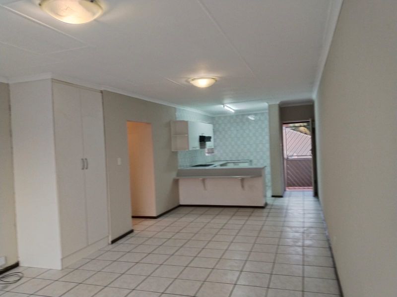 An open-plan living and kitchen area featuring tiled flooring, built-in cabinetry, and a breakfast bar, offering a clean and functional layout.