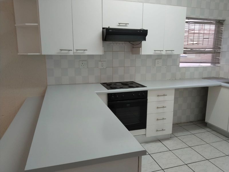 A clean and functional kitchen featuring white cabinetry, laminate countertops, a built-in oven with hob, and a tiled backsplash.