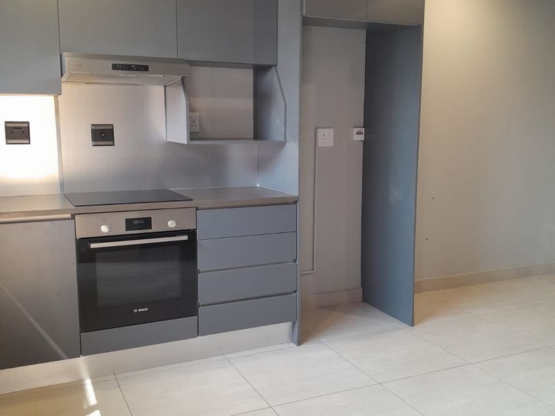 Modern kitchen featuring sleek grey cabinetry, stainless steel splashback, integrated oven and hob, and neutral tiled flooring in an open-plan layout.