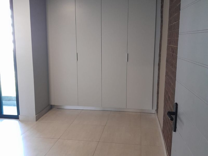 A bright, empty bedroom featuring modern tiled flooring, built-in cupboards, and an attractive exposed brick feature wall with access to an outdoor area.
