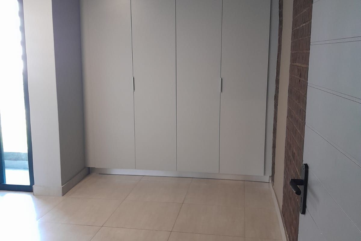 A bright, empty bedroom featuring modern tiled flooring, built-in cupboards, and an attractive exposed brick feature wall with access to an outdoor area.