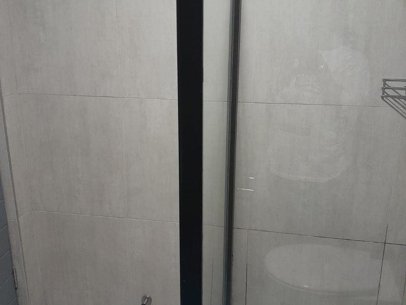 A modern bathroom shower area featuring light-toned wall and floor tiles with a sleek black-framed glass shower enclosure.