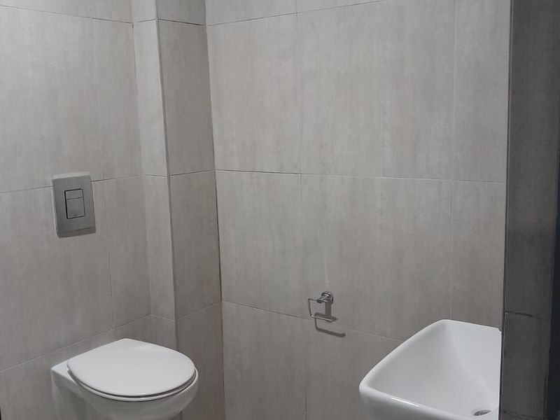 A modern, minimalist bathroom featuring neutral wall-to-wall tiling, a wall-mounted toilet with a concealed cistern, and a compact basin.