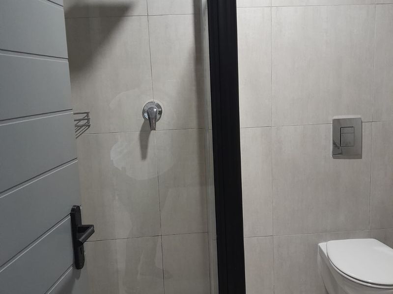 Modern bathroom featuring a wall-mounted toilet, walk-in shower with black frame, and neutral wall tiling.