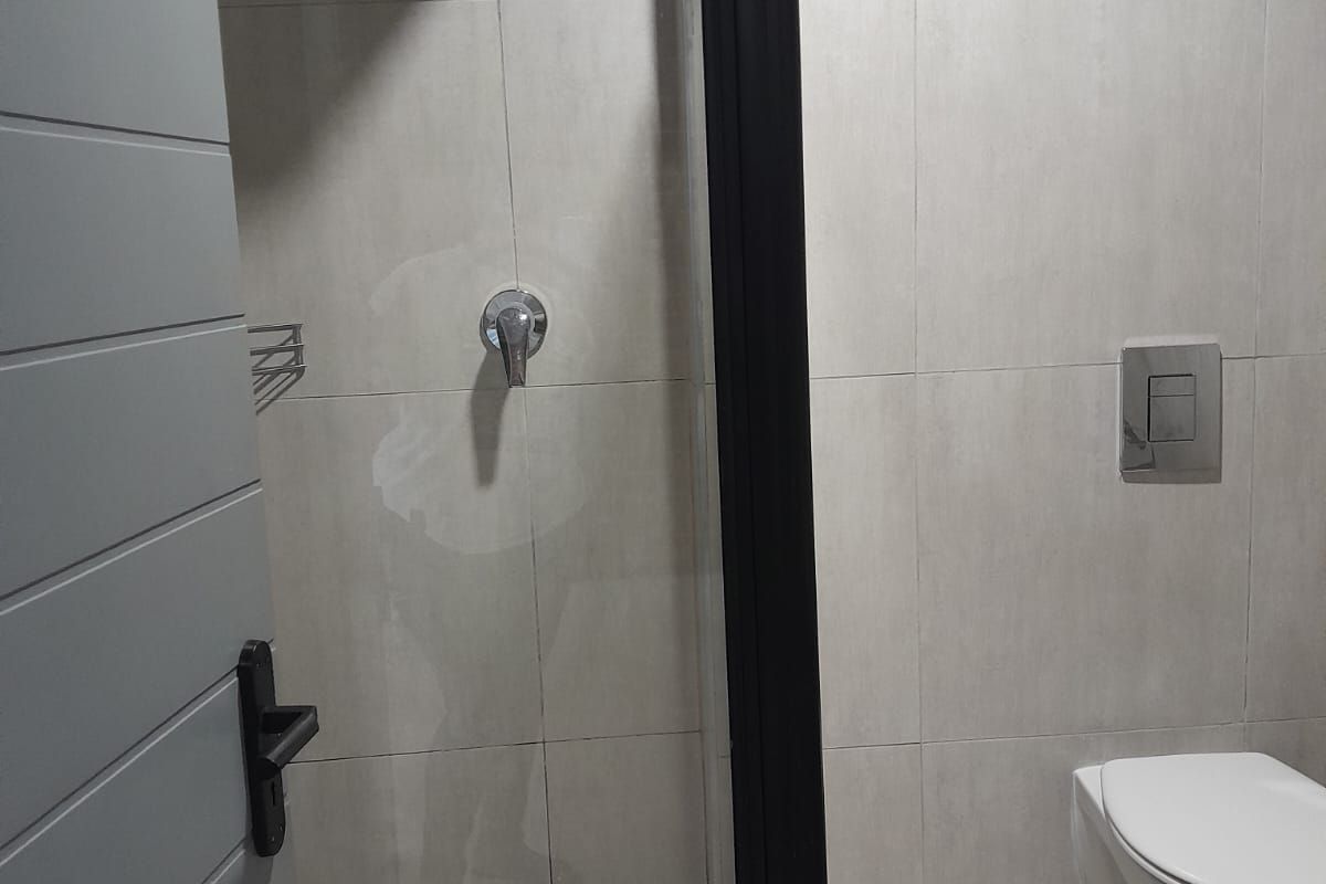 Modern bathroom featuring a wall-mounted toilet, walk-in shower with black frame, and neutral wall tiling.