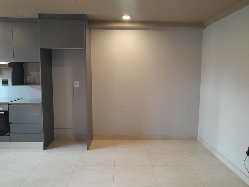 Modern kitchen area featuring grey built-in cabinetry, integrated oven, hob, and extractor fan with neutral tiled flooring and recessed lighting.