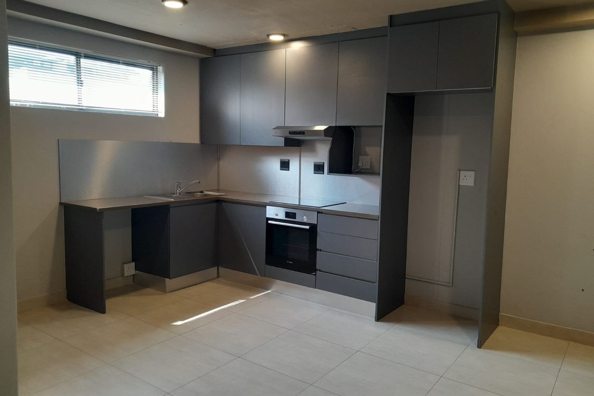 Modern kitchen featuring sleek grey cabinetry, stainless steel splashbacks, integrated oven, electric hob, and tiled flooring in an open-plan layout.