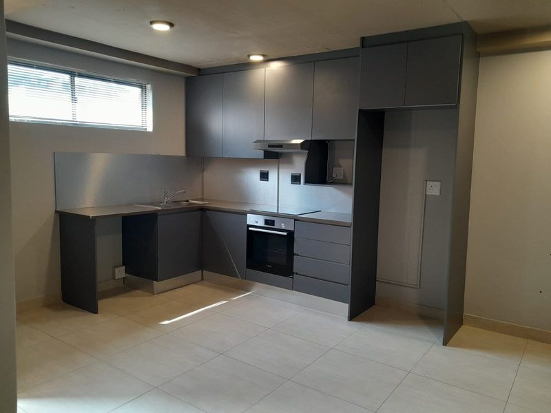 Modern kitchen featuring sleek grey cabinetry, stainless steel splashbacks, integrated oven, electric hob, and tiled flooring in an open-plan layout.