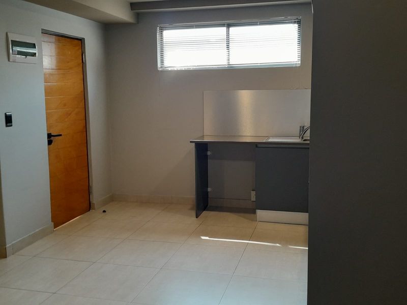 A compact kitchen area featuring a stainless steel countertop, integrated sink, and tiled flooring, currently requiring cabinetry completion and finishing touches.