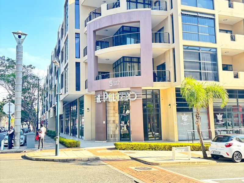 Street-level view of the modern El Palazzo apartment building featuring a prominent glass facade, multiple balconies, and a paved entrance area.