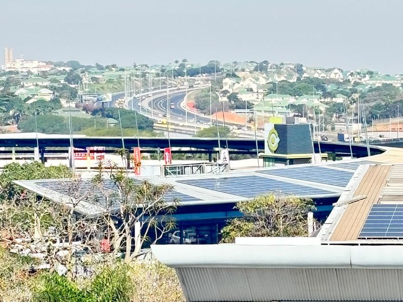 Elevated view overlooking the surrounding neighborhood, highway infrastructure, and nearby commercial buildings with solar panel installations on the roof.