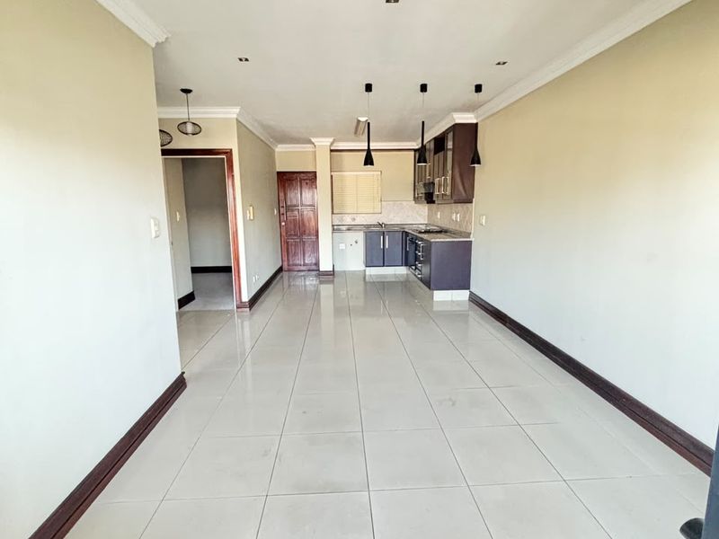 Spacious open-plan living area featuring tiled flooring, recessed lighting, and a functional kitchen with built-in cabinetry and appliances.