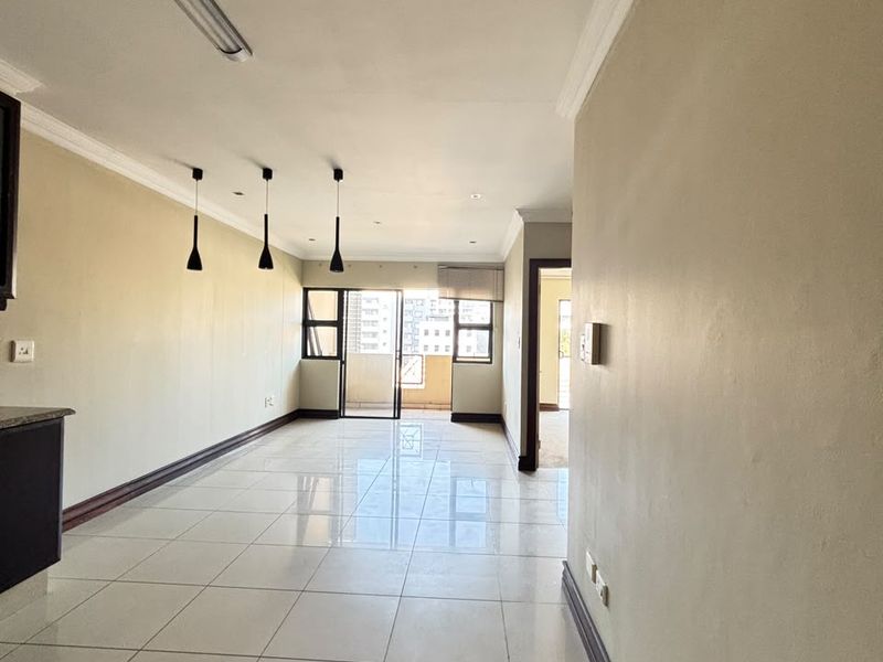 Spacious open-plan living area featuring neutral walls, polished tiled flooring, modern pendant lighting, and direct access to a private balcony.
